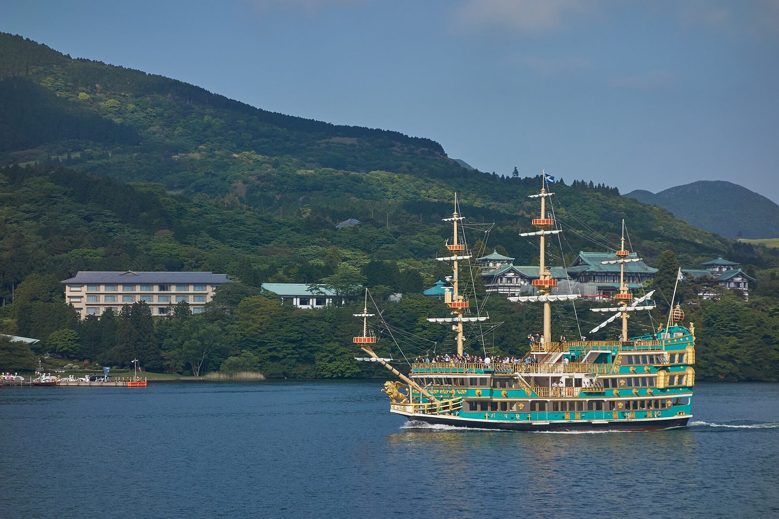 เรือโจรสลัดสีสดล่องในทะเลสาบอาชิ มีภูเขาเขียวเป็นฉากหลัง